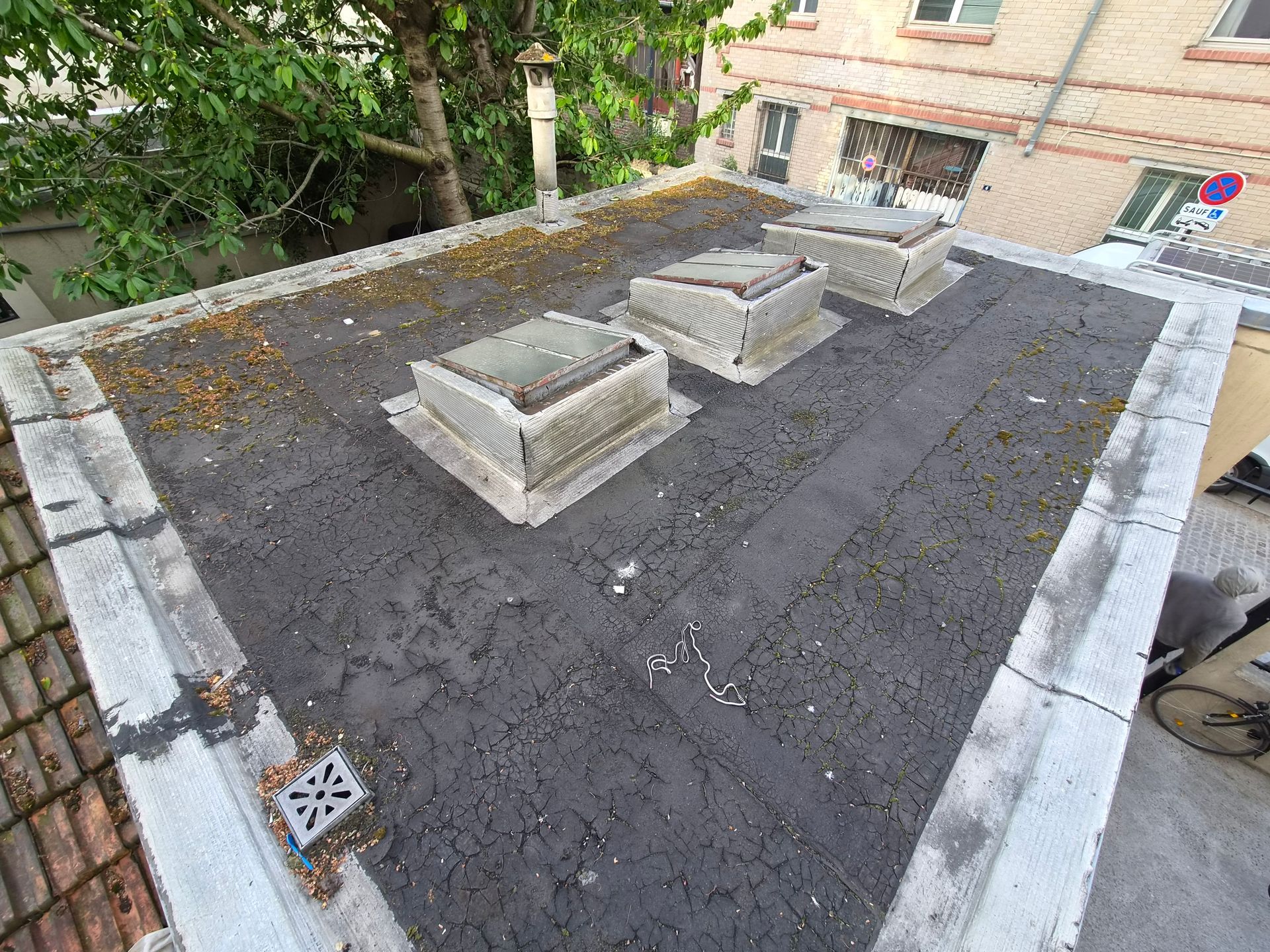 Un ouvrier casqué avec un harnais nettoie un toit en tuiles au nettoyeur haute pression.