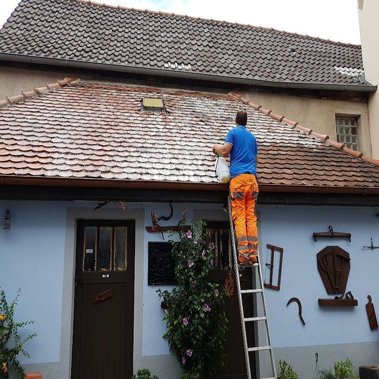 Un couvreur applique un traitement à l'aide d'un pulvérisateur, sur une toiture.