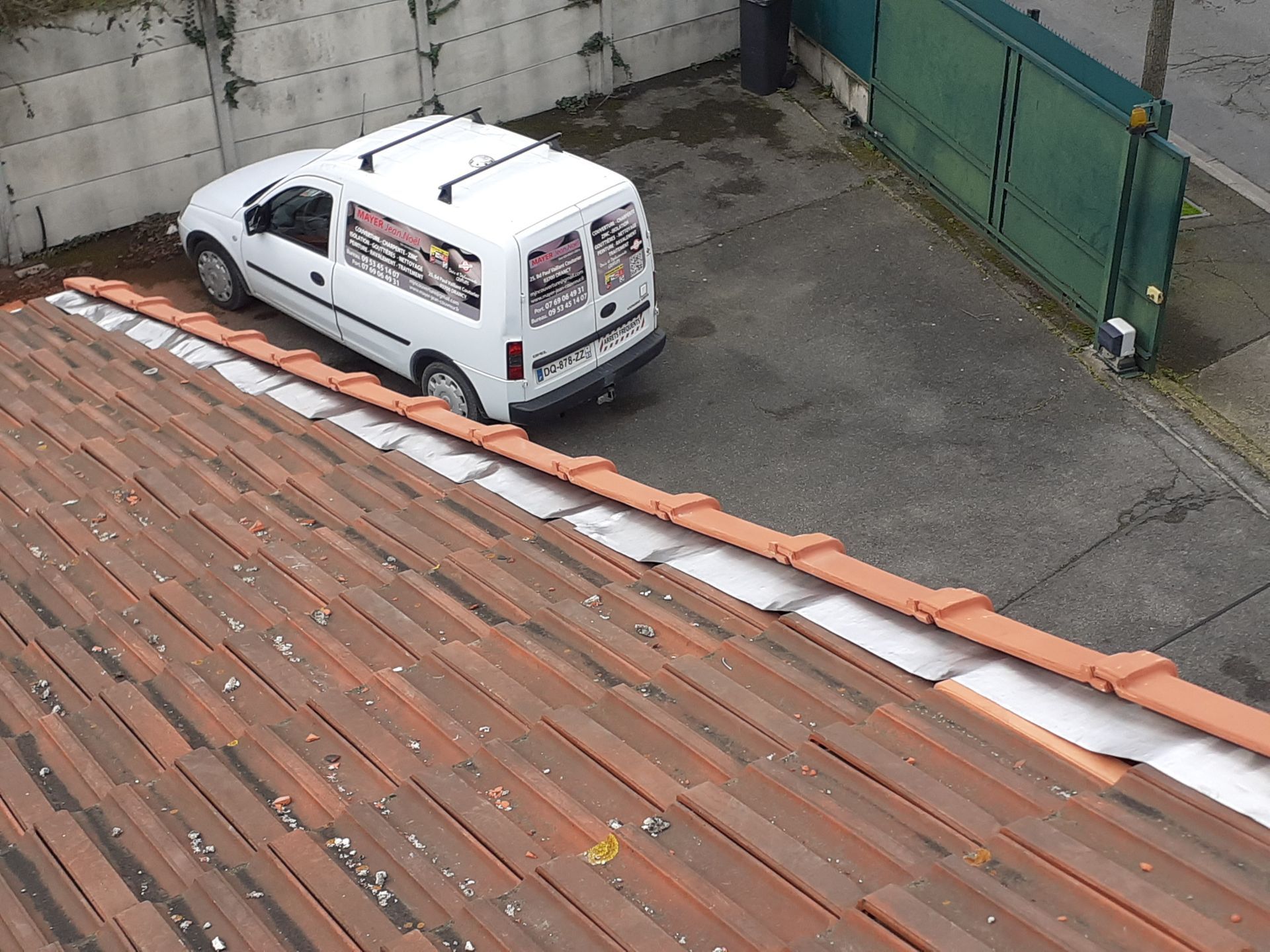Vue d'un toit d'une camionnette blanche garée sur un parking à côté d'un portail vert.