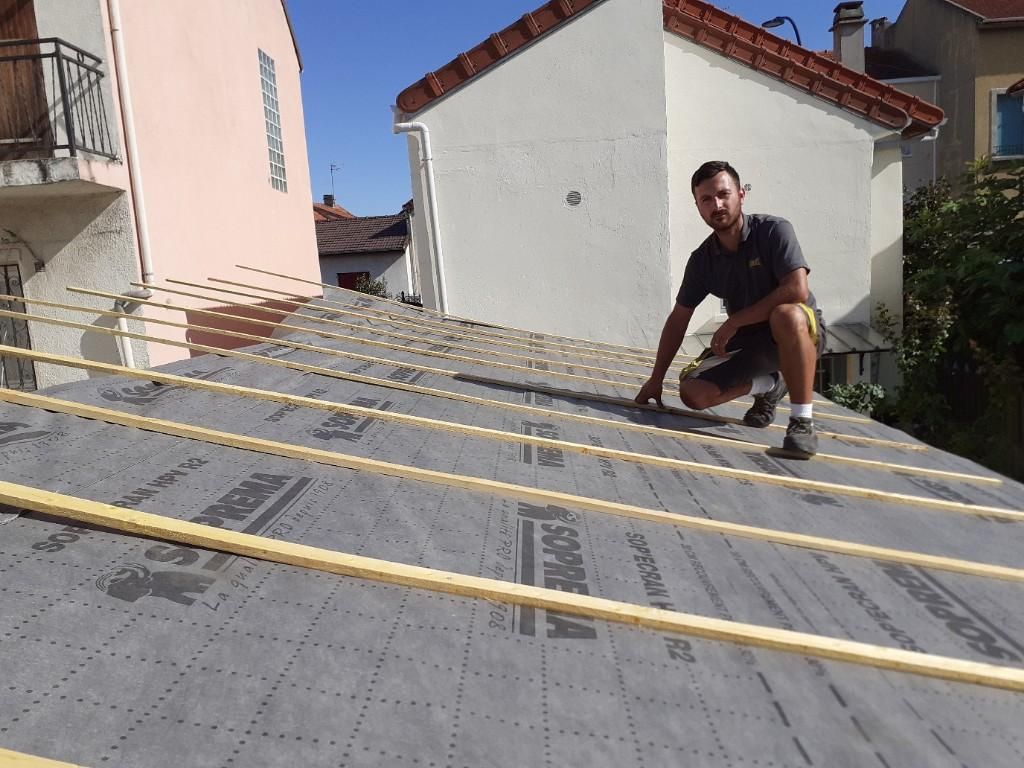 Un homme accroupi sur un toit pose l'isolation d'une toiture.