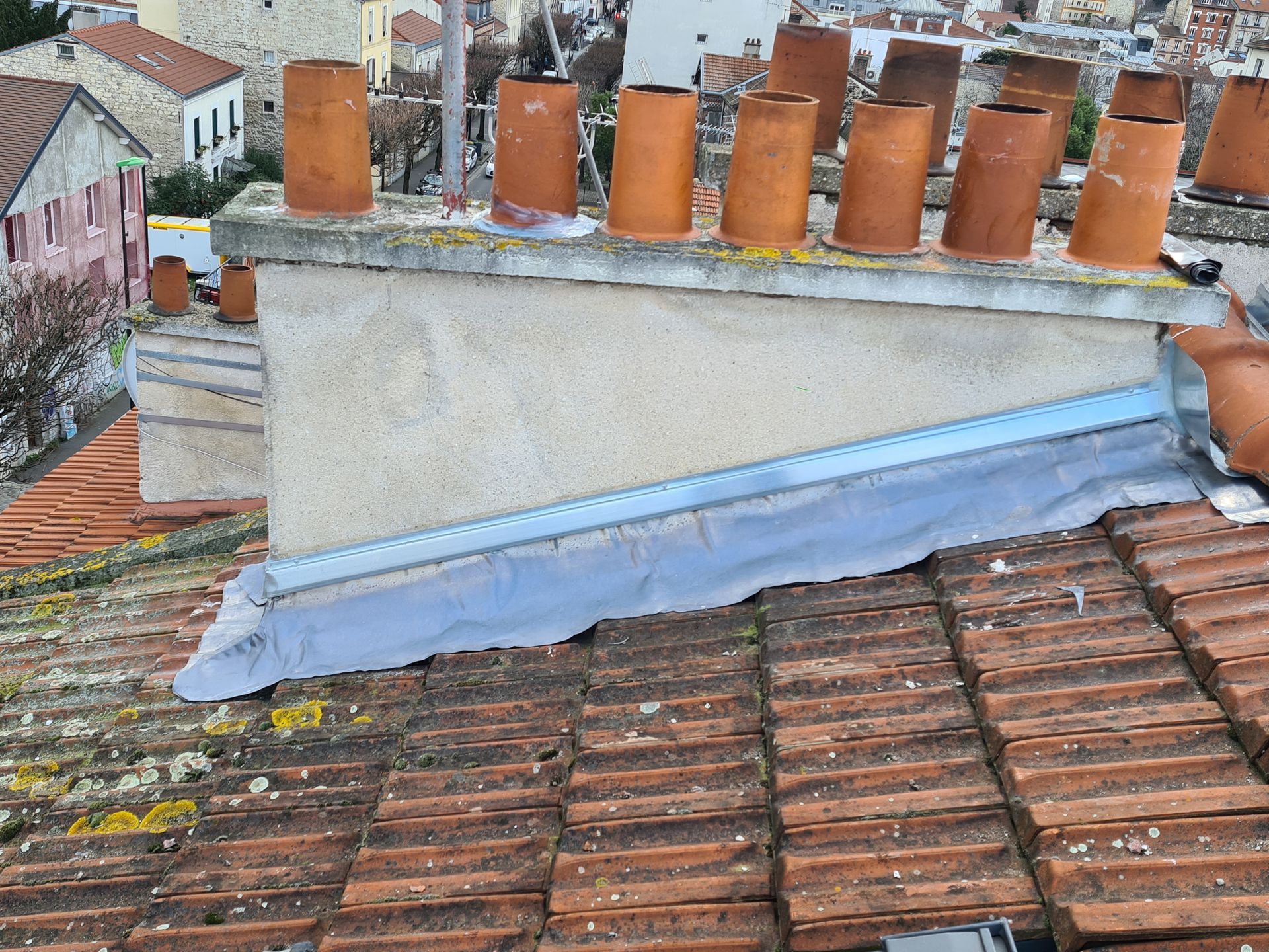 Toiture avec cheminées et solins en zinc recouvrant des tuiles en terre cuite rouge.