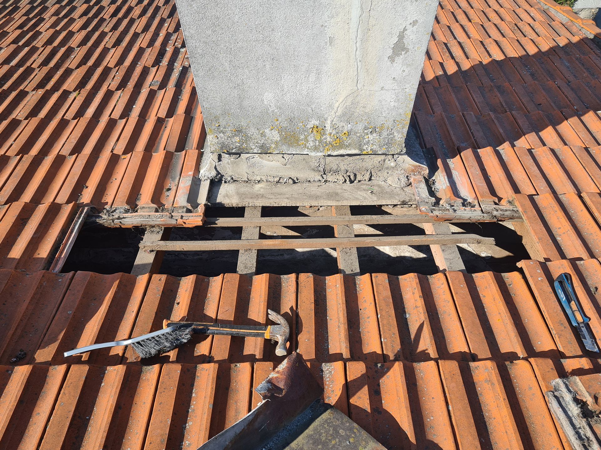 Toiture avec tuiles avec une section endommagée autour d'une cheminée en béton.