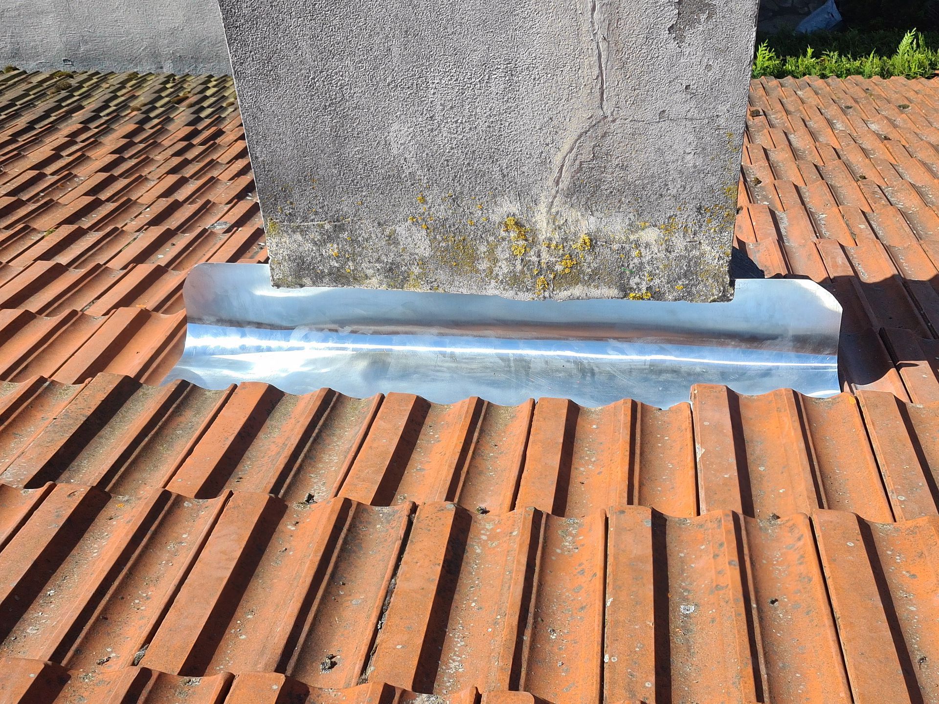 Gros plan sur la base d'une cheminée de toit avec un solin en zinc sur des tuiles en terre cuite rouge.