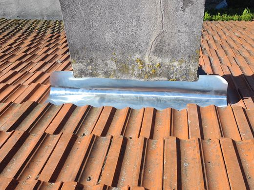 Cheminée en pierre avec un solin en zinc sur un toit de tuiles rouges.