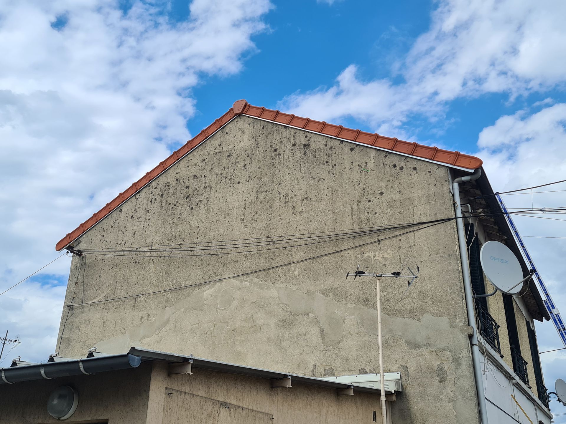 Maison en stuc patiné par le temps, au toit de tuiles rouges, sous un ciel bleu partiellement nuageux.