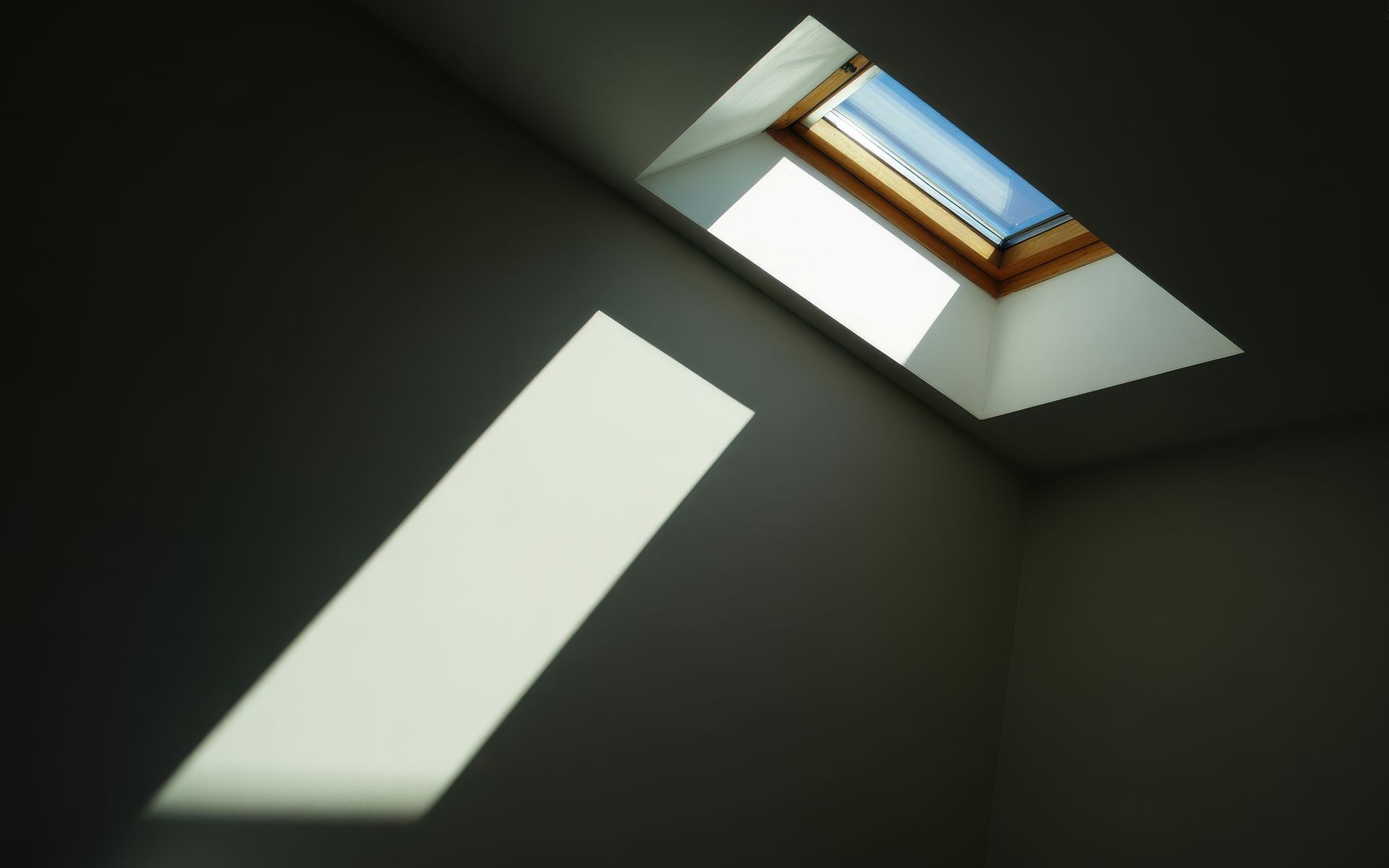 Pièce sombre avec un puits de lumière projetant un faisceau rectangulaire sur un mur sombre.
