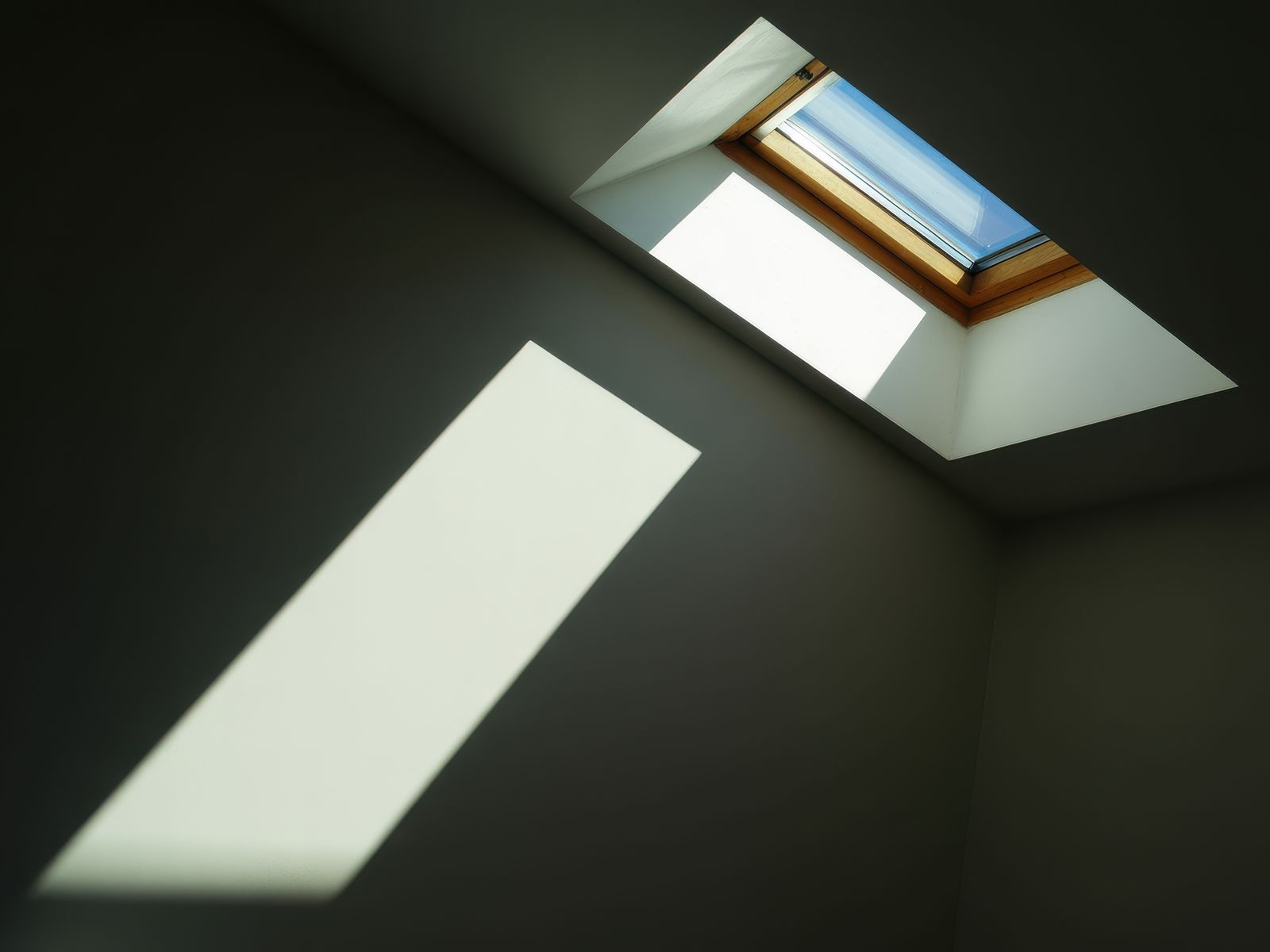 Pièce sombre avec un puits de lumière projetant un faisceau rectangulaire sur un mur sombre.