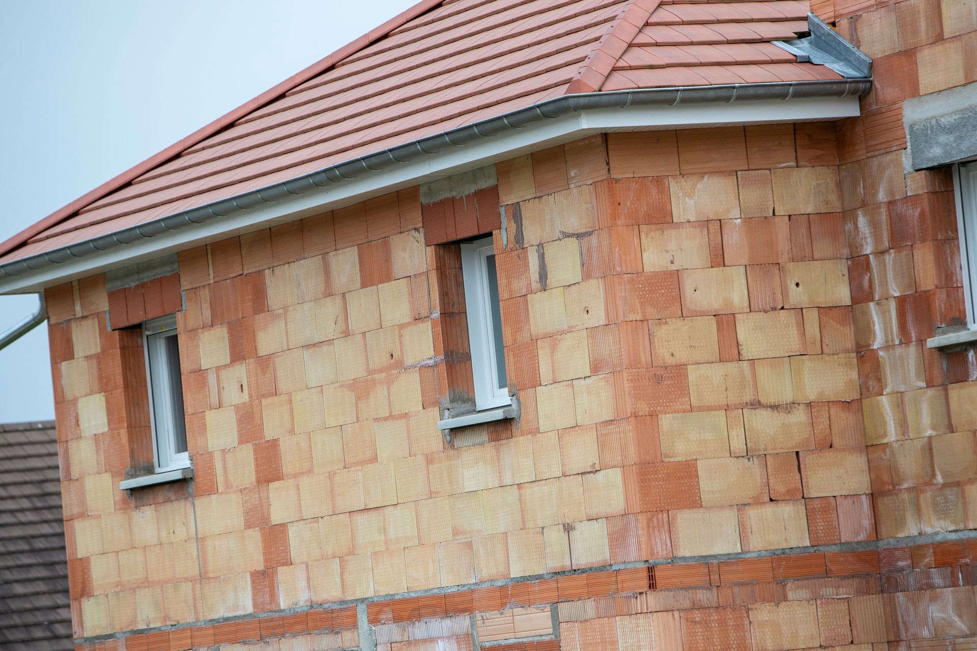 Maison en construction, avec un toit de tuiles rouges et des murs inachevés.