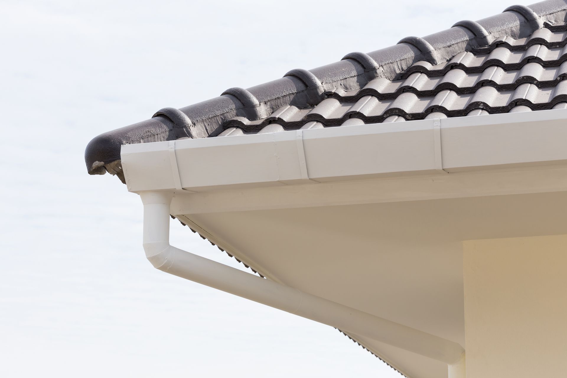Gros plan sur le toit d'une maison aux tuiles grises et aux gouttières blanches.