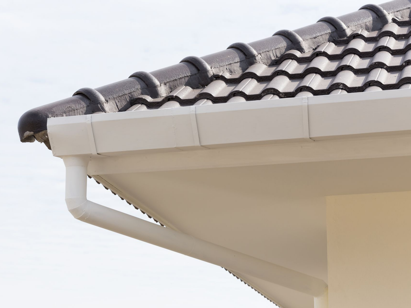 Avant-toit d'une maison blanche avec toit de tuiles grises et gouttières.