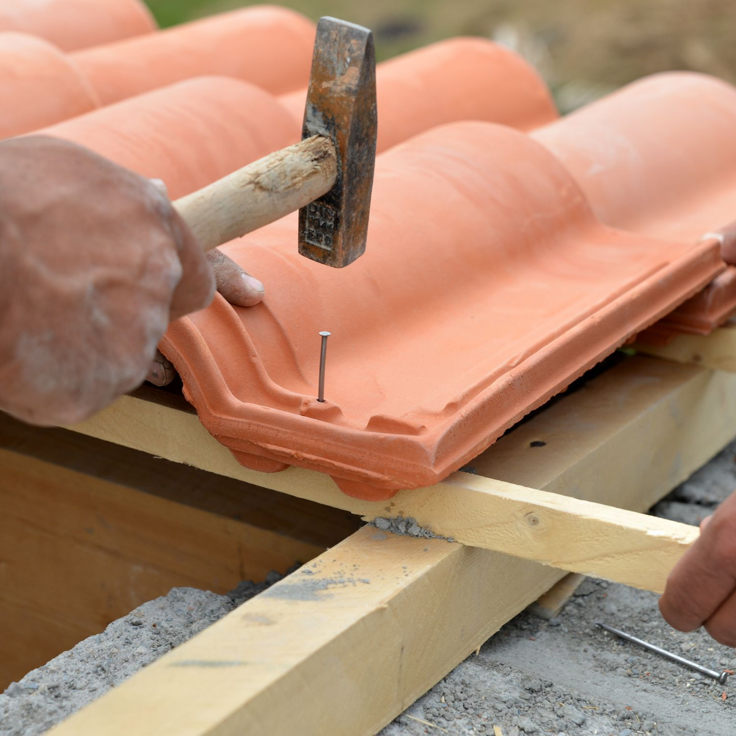 Enfoncer un clou dans des tuiles de toit en terre cuite à l'aide d'un marteau lors de travaux de réparation.