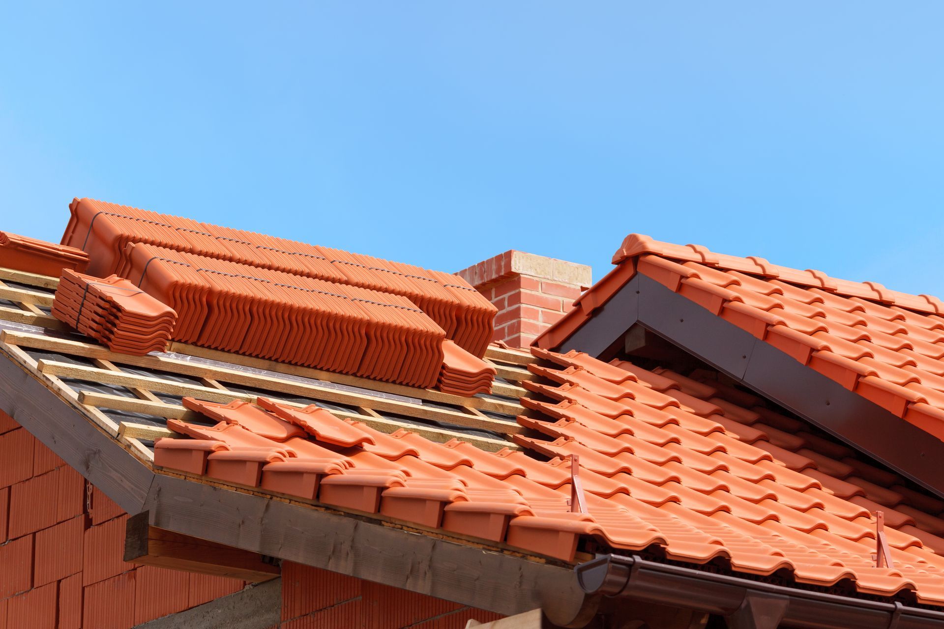 Tuiles de terre cuite rouge et matériaux de couverture empilés sur une maison sous un ciel bleu clair.