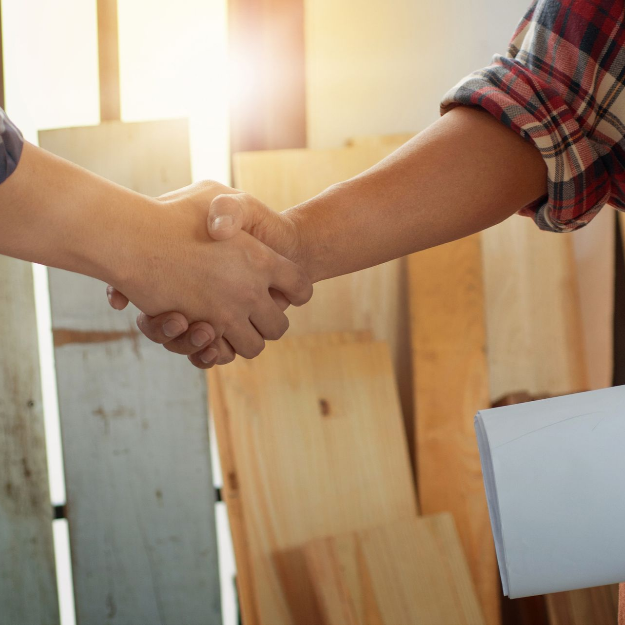 Deux personnes se serrent la main dans un atelier, avec des planches en bois en arrière-plan.