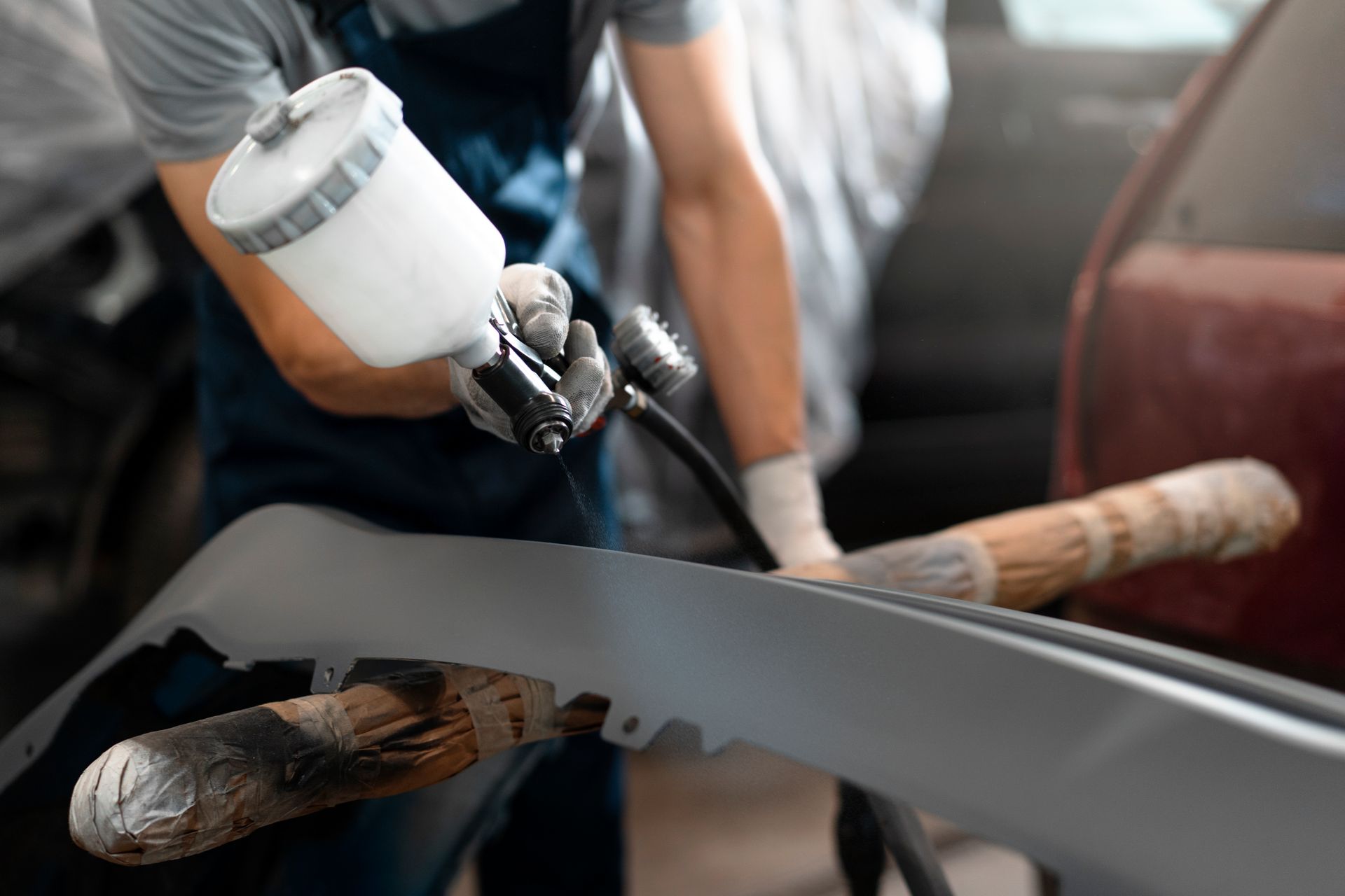 Un hombre está pintando con aerosol el parachoques de un automóvil en un garaje.