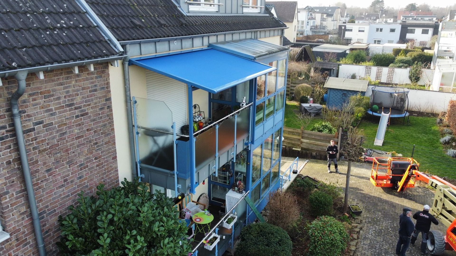 Zweistöckiges Gebäude mit blauen Akzenten, Glaswänden und einer blauen Markise, mit Blick auf einen Hinterhof