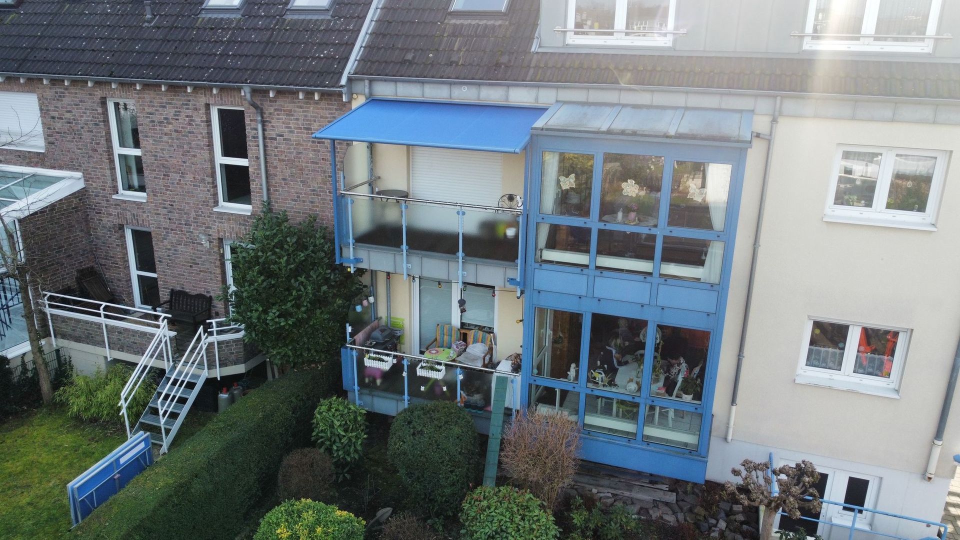 Außenansicht eines blau-verglasten Gebäudes mit Balkonen, neben einem Backsteingebäude.