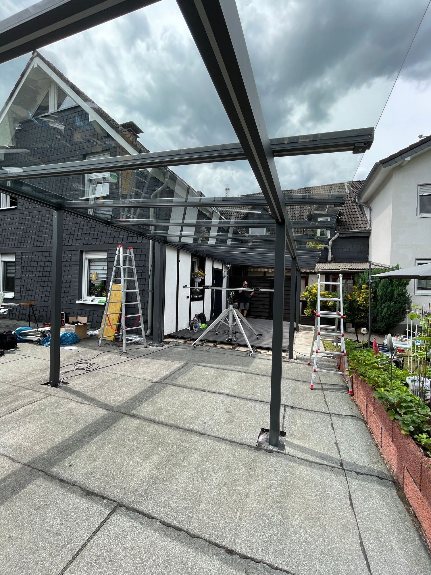 Errichtung einer Terrassenüberdachung aus Glas und Metall mit Leitern auf einer gepflasterten Terrasse.
