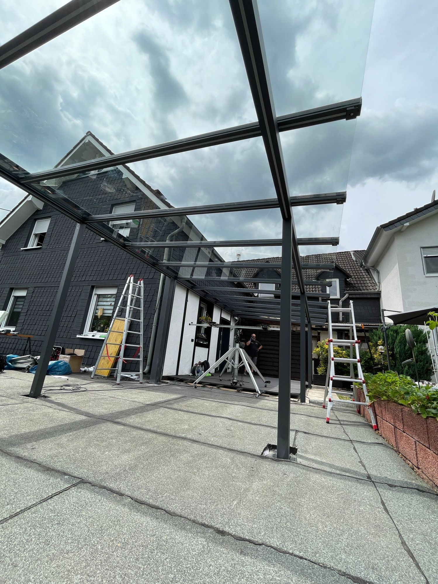 Bau eines modernen Carports mit schwarzen Stützen und Glasdach neben einem Backsteinhaus.