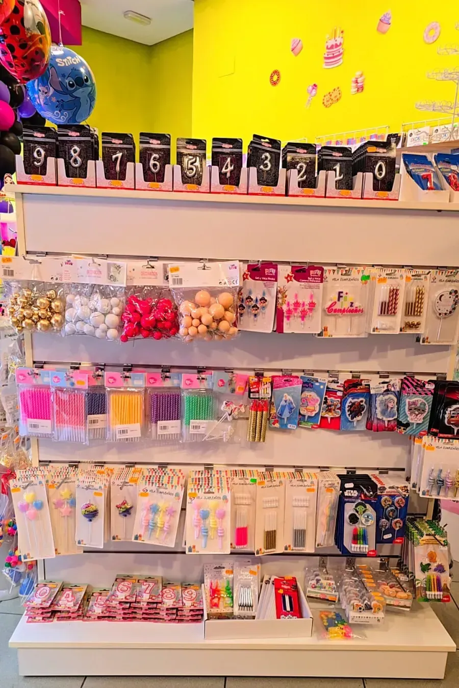 Estantes llenos de suministros para fiestas, incluidas velas, globos y decoraciones.