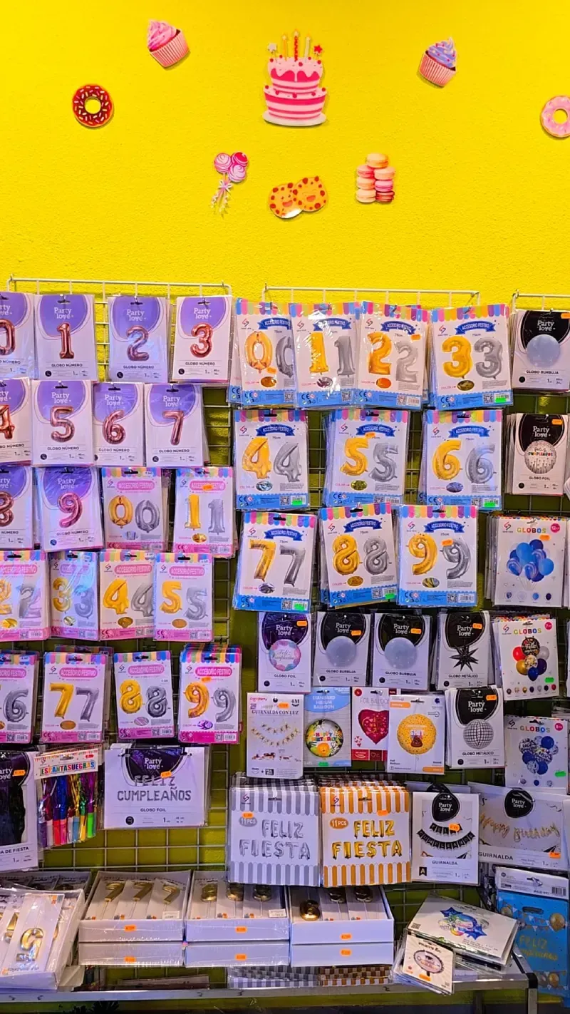 Estantes llenos de globos con forma de números y decoraciones festivas contra una pared amarilla.