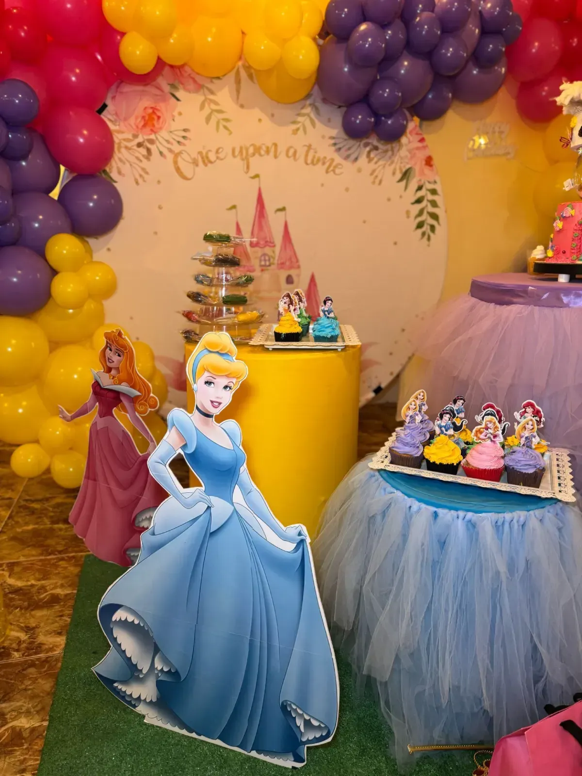 Fiesta temática de Cenicienta con globos, pastel y exhibición de cupcakes; el recorte de Cenicienta está en primer plano.