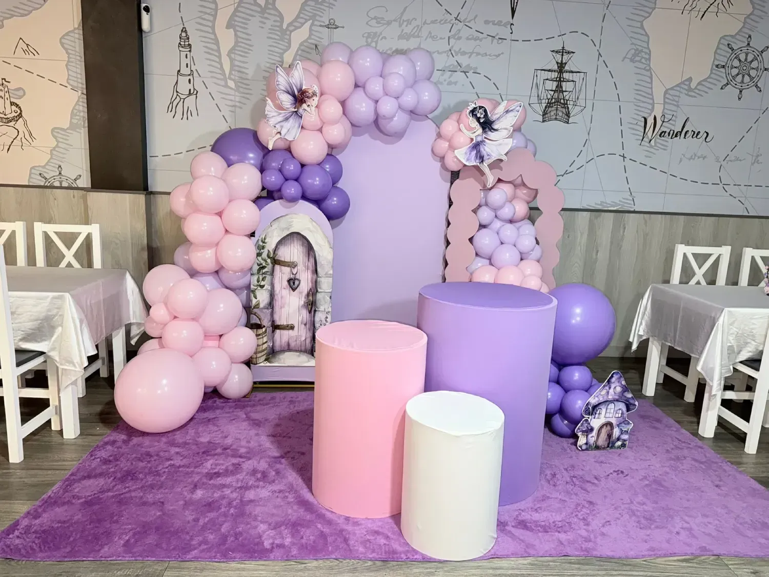 Fondo de fiesta morado y rosa con globos, pedestales y una puerta con temática de hadas.