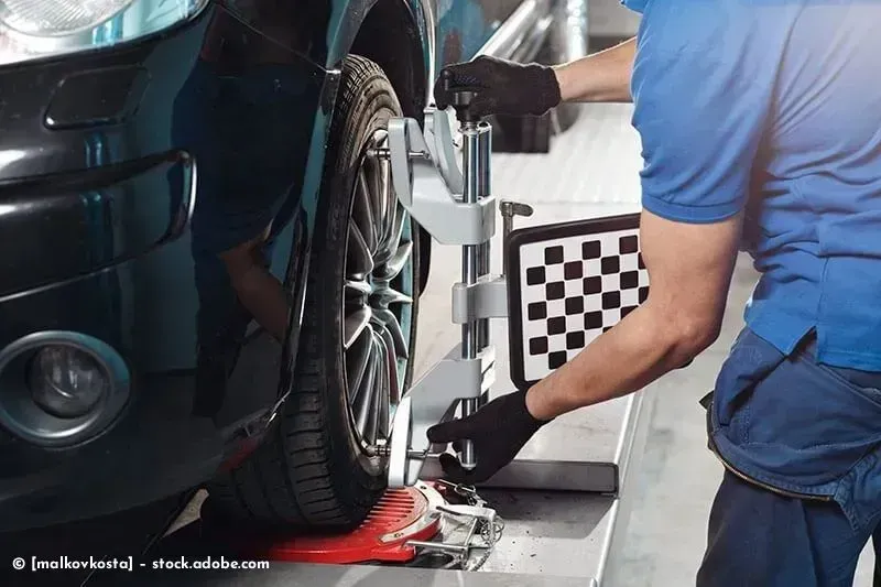Ein Mechaniker justiert ein Autorad auf einer Achsmessanlage in einer Werkstatt.