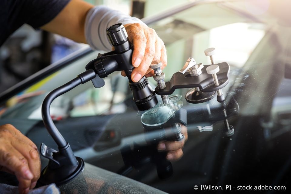 Ein Techniker repariert im Inneren eines Autos eine gesprungene Windschutzscheibe mit einem Saugnapfwerkzeug.