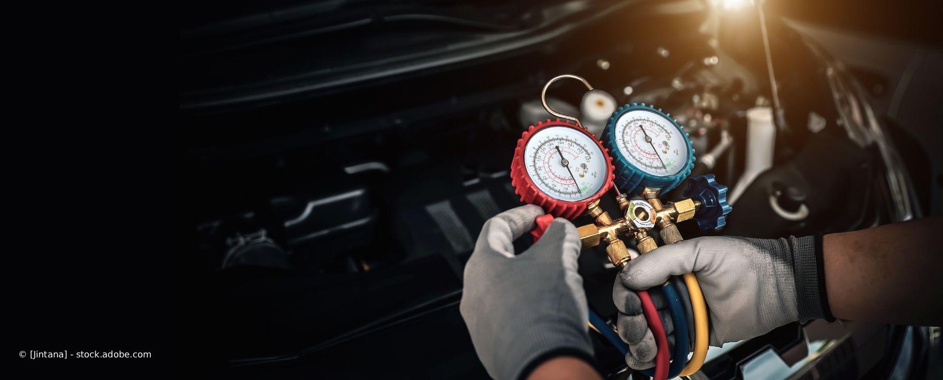 Behandschuhte Hände justieren rote und blaue Anzeigen an einem Klimaanlagenverteiler in einem dunklen Motorraum