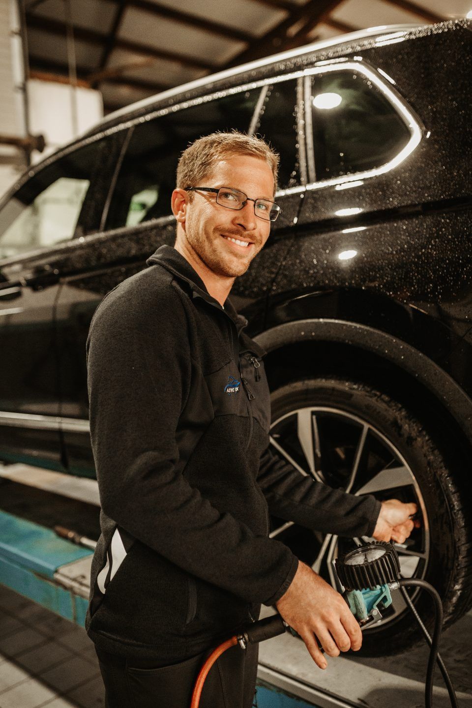 Ein Mechaniker überprüft in einer Garage einen Reifen an einem schwarzen SUV.