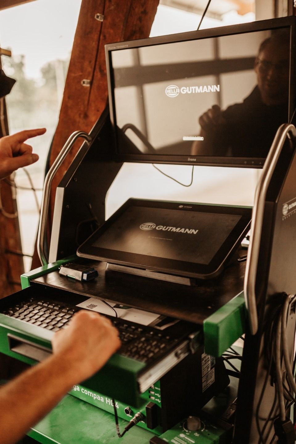 Laptop-Kiosk mit Tastatur und zwei Monitoren auf einem grünen Gerätegestell in einem Zelt- oder Messestandaufbau