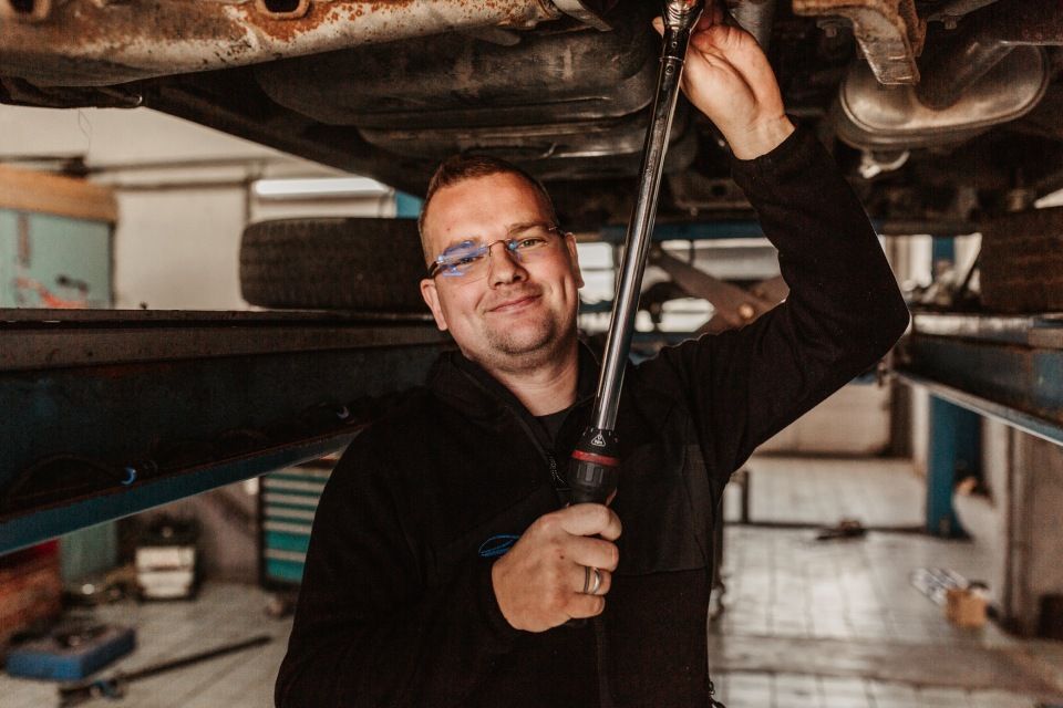 Ein Mechaniker benutzt einen Schraubenschlüssel unter einem auf einer Hebebühne stehenden Auto in einer Autowerkstatt.