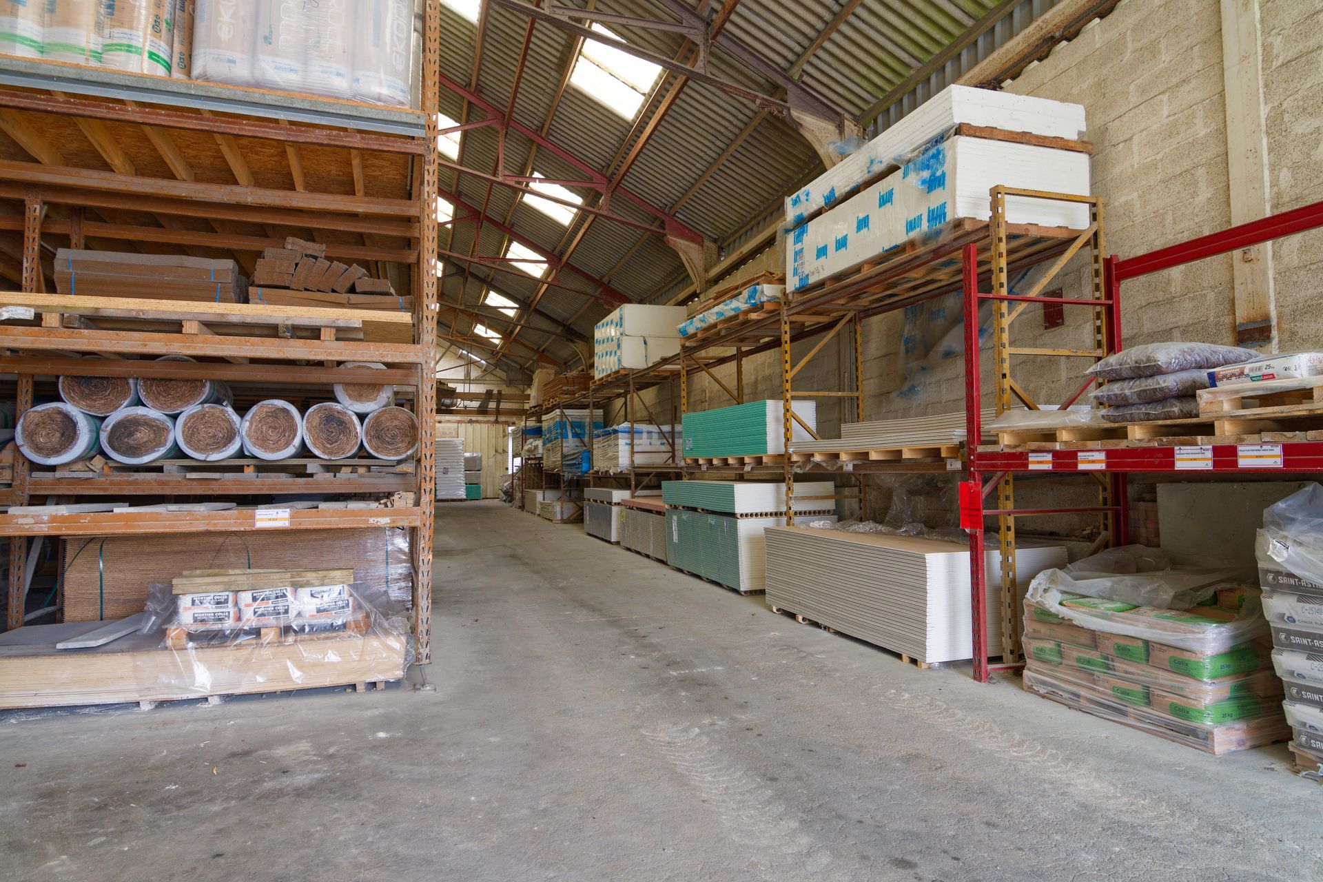 Intérieur d'entrepôt avec rangées d'étagères contenant des matériaux de construction, y compris des cloisons sèches.