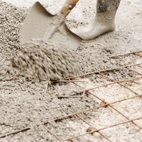 Pelleter du béton humide sur une grille en treillis métallique ; personne portant des bottes.