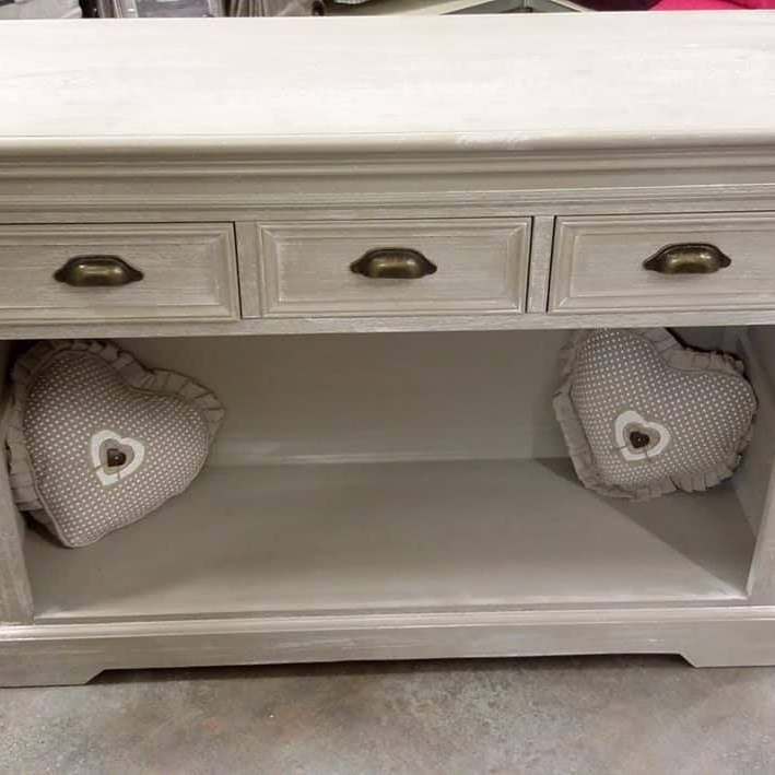Console en bois blanc cassé avec trois tiroirs et coussins en forme de cœur dans l'espace ouvert.