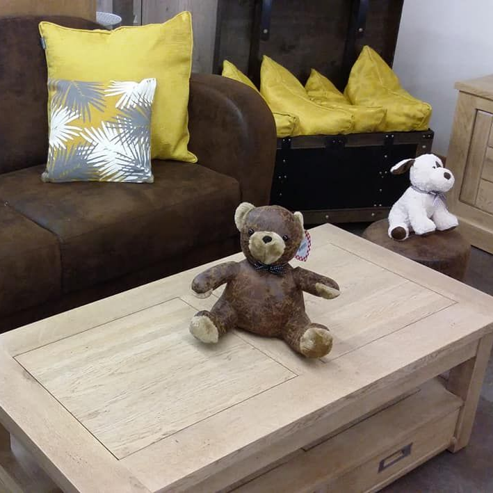 Ours en peluche sur une table basse en bois clair, canapé en cuir marron avec coussins jaunes.