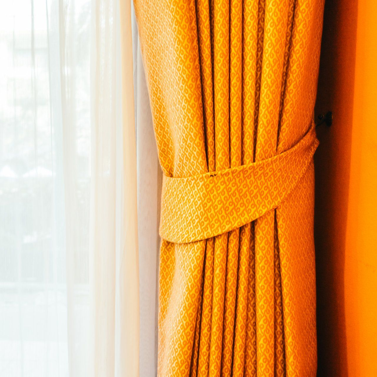 Rideau à motifs orange noué en arrière, à côté d'un rideau blanc transparent près d'une fenêtre.