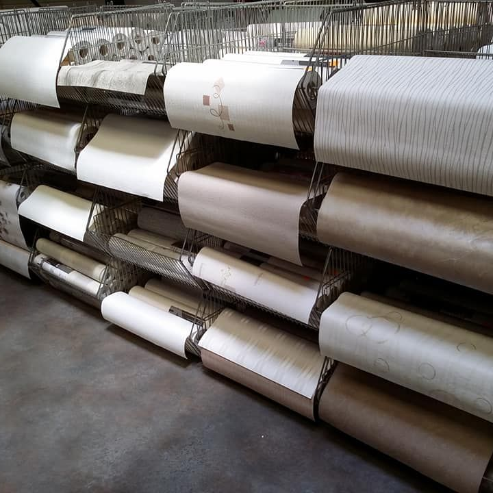 Rouleaux de papier peint de différentes couleurs et motifs rangés dans un support en métal.