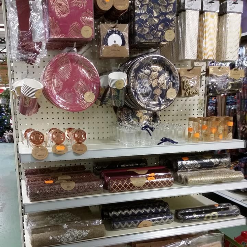 Étagères dans un magasin présentant des fournitures de fête, notamment des assiettes, des coffrets cadeaux et du papier d'emballage.