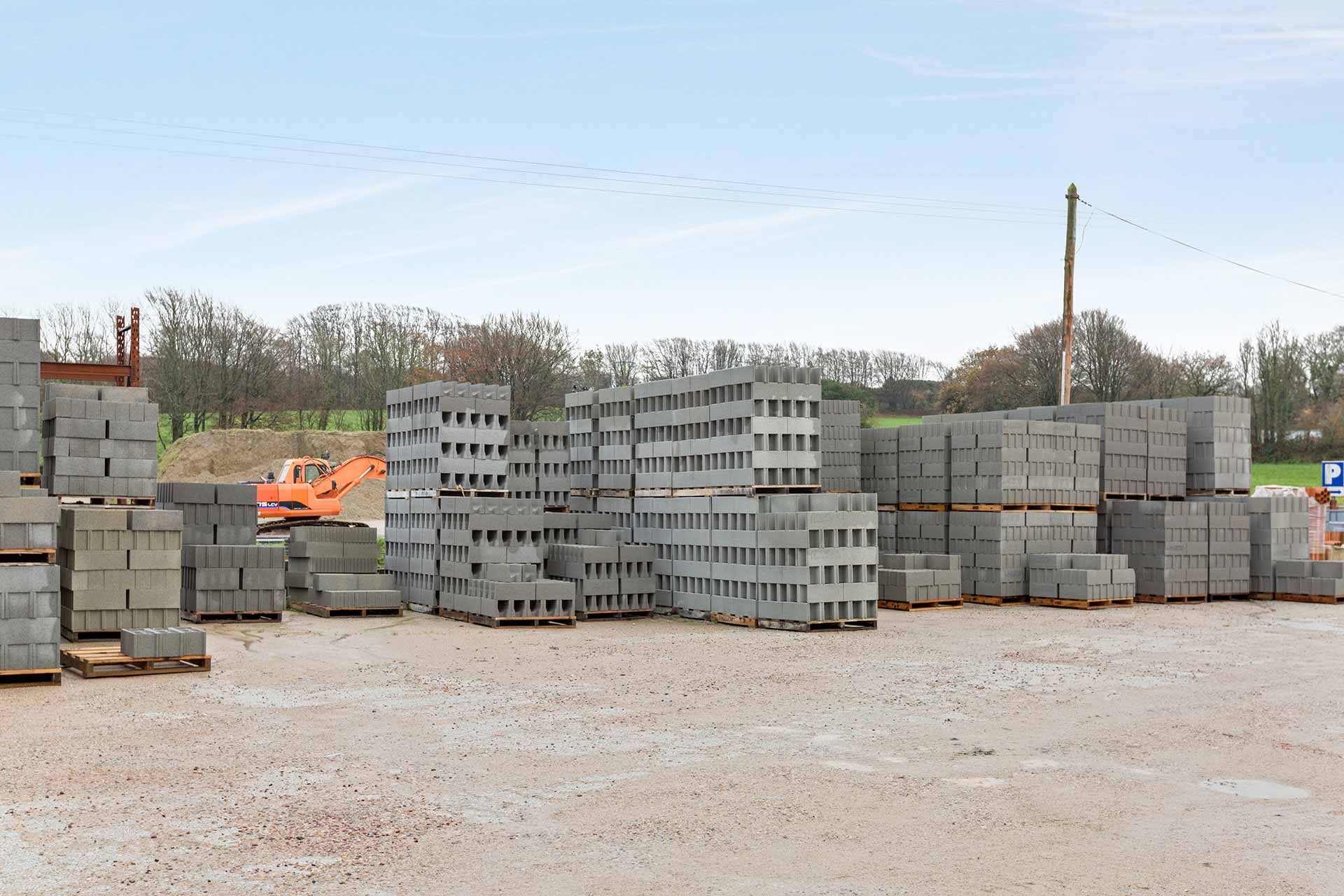 Piles de parpaings gris sur des palettes dans une cour de matériaux de construction extérieure.