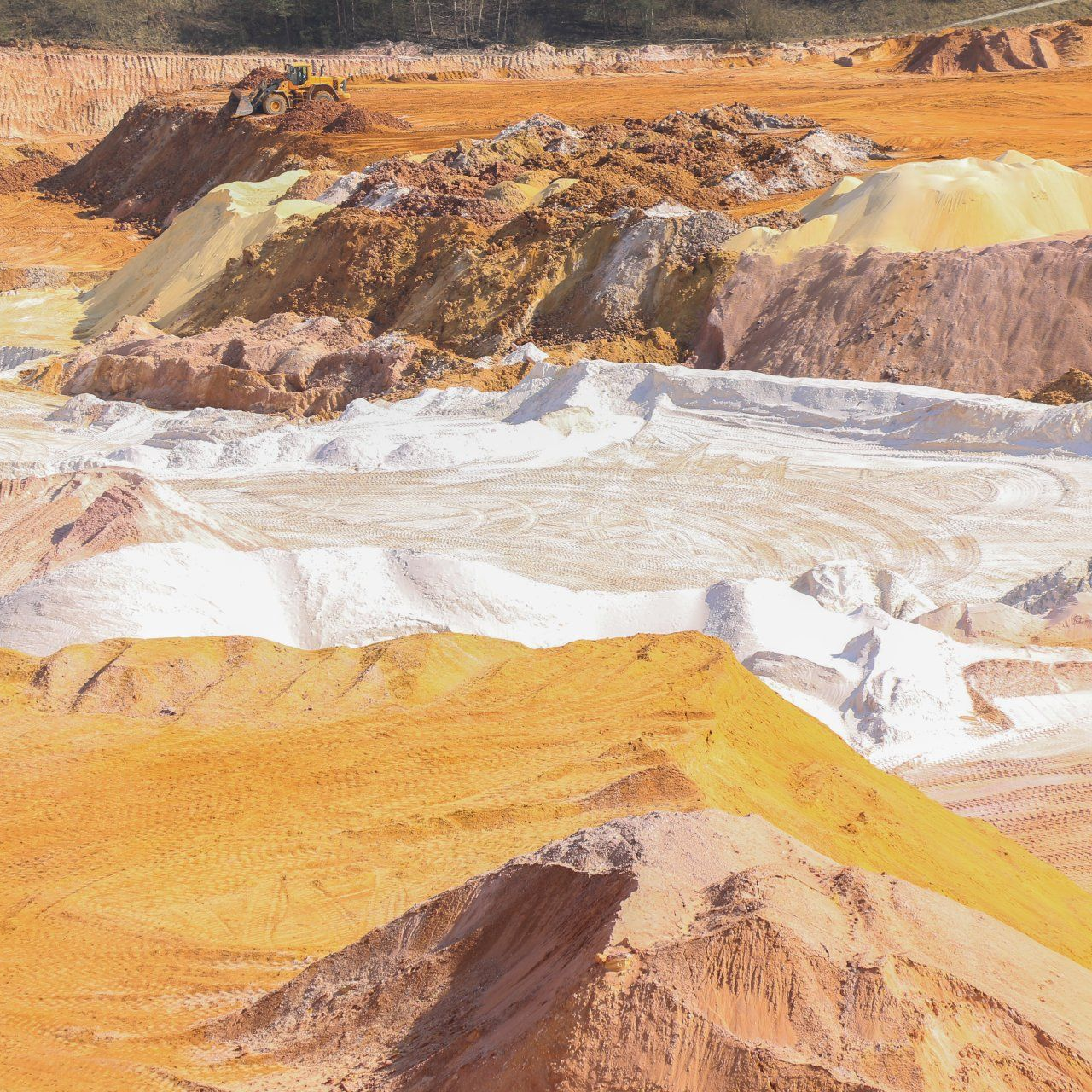 Monticules de terre de différentes couleurs : orange, blanc et marron, probablement dans une carrière ou une exploitation minière.