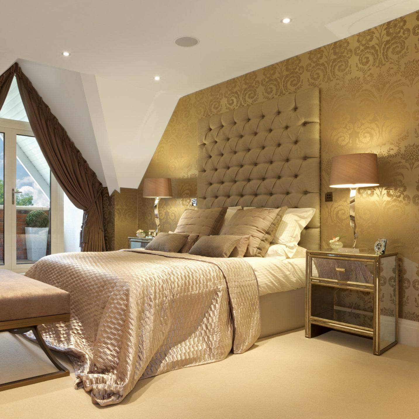 Chambre élégante avec des accents dorés, une tête de lit capitonnée, des lampes de chevet et un accès au balcon.