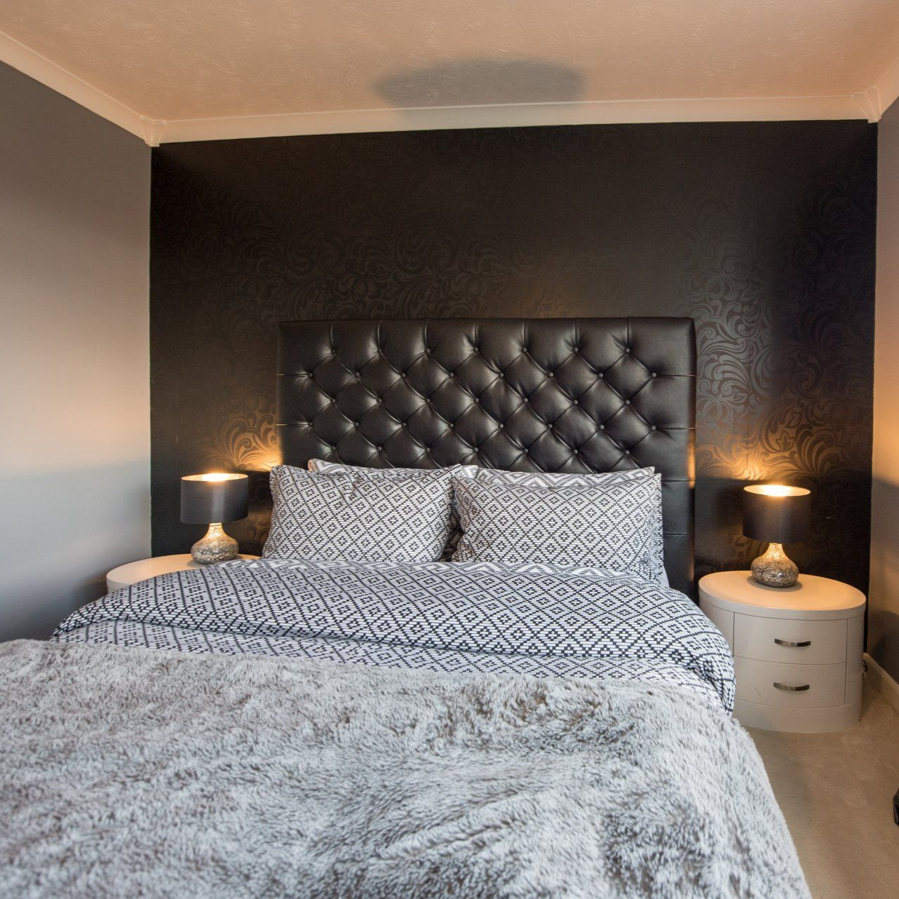 Chambre avec mur d'accent noir, lit avec literie grise et tête de lit capitonnée, lampes sur tables de chevet.