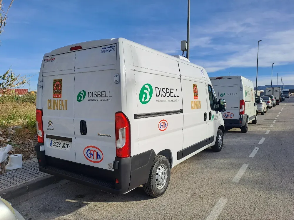 Furgonetas blancas con logotipos verdes estacionadas al costado de una carretera bajo un cielo azul.