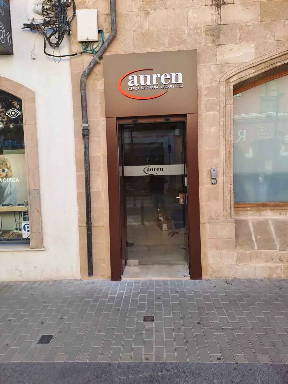 Entrada al negocio de Auren con puerta de vidrio, marco marrón y logotipo en el cartel.