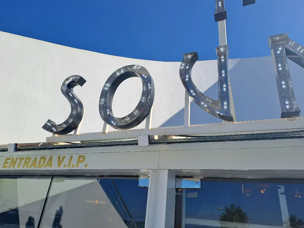 "Señal SOL con luces integradas, sobre estructura blanca, cartel 'Entrada VIP', cielo azul".