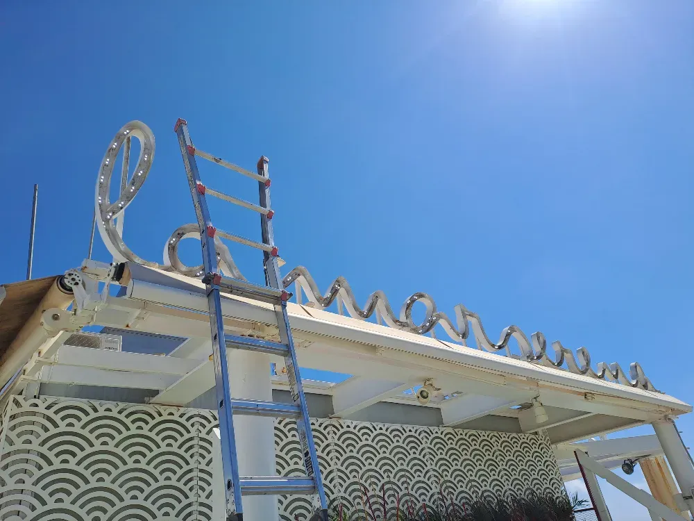 Escalera apoyada sobre una estructura blanca con un diseño recortado ornamentado y un cartel parcialmente iluminado