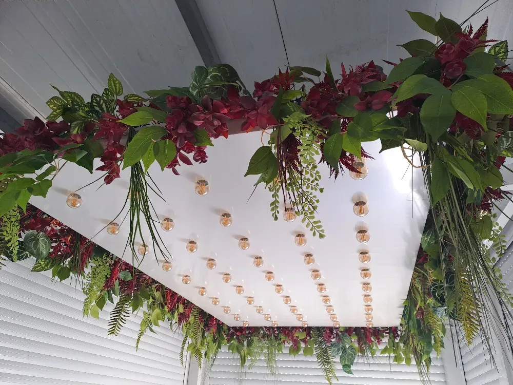 Estructura rectangular blanca con follaje decorativo rojo y verde y luces doradas suspendidas de un techo blanco.