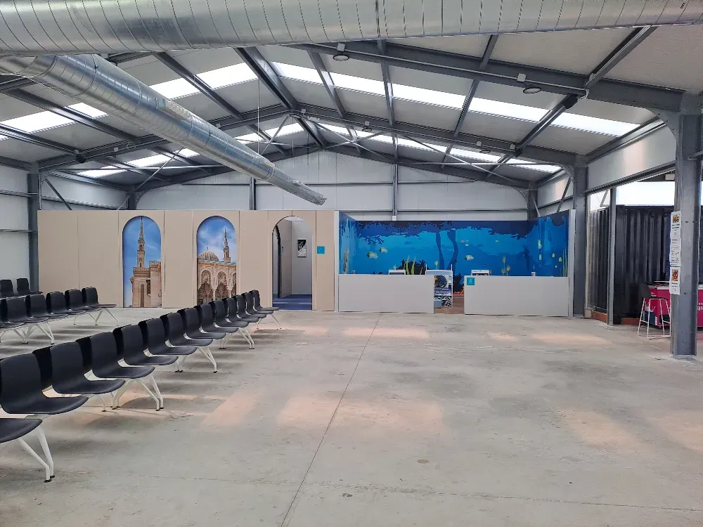 Interior de un gran edificio con filas de sillas, fondos de pantalla y techo abierto.