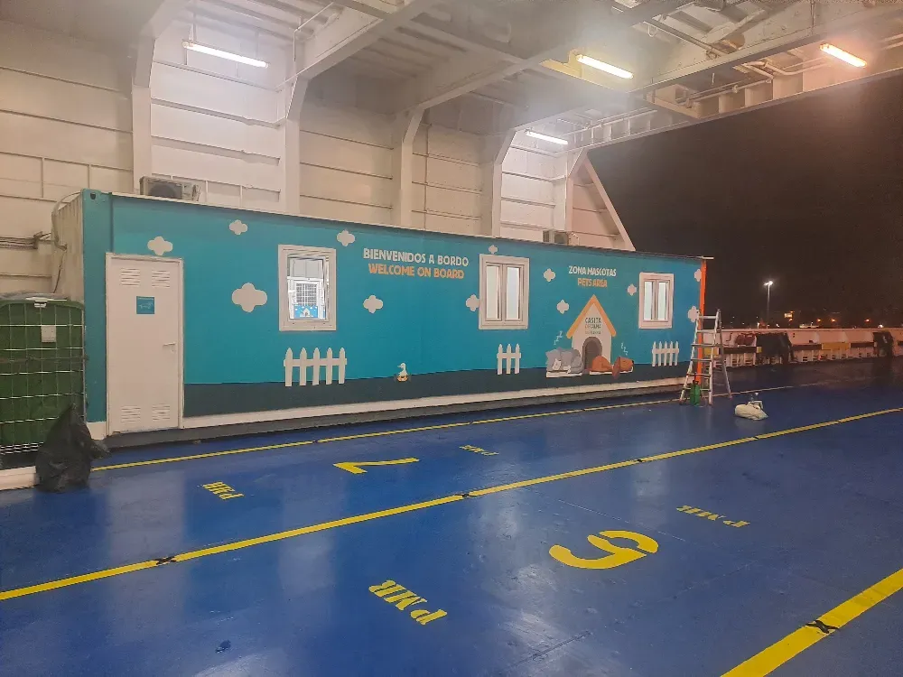 Un contenedor verde azulado con ilustraciones de dibujos animados se encuentra en la cubierta de un ferry. 